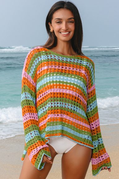 Smiling woman in a colorful striped sweater, standing on a beach by the ocean.