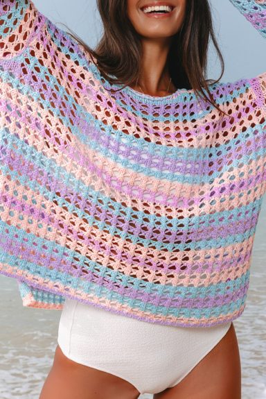 Woman wearing a colorful, cropped knit sweater over a white swimsuit, smiling by the beach.